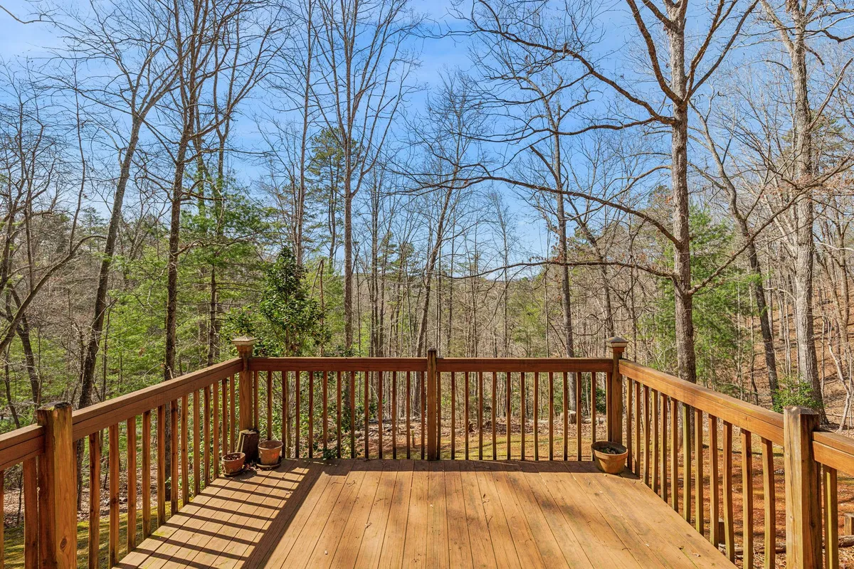 This image features a spacious wooden deck surrounded by trees and blue sky, with comfortable outdoor seating inviting guests to relax and enjoy the peaceful natural environment.