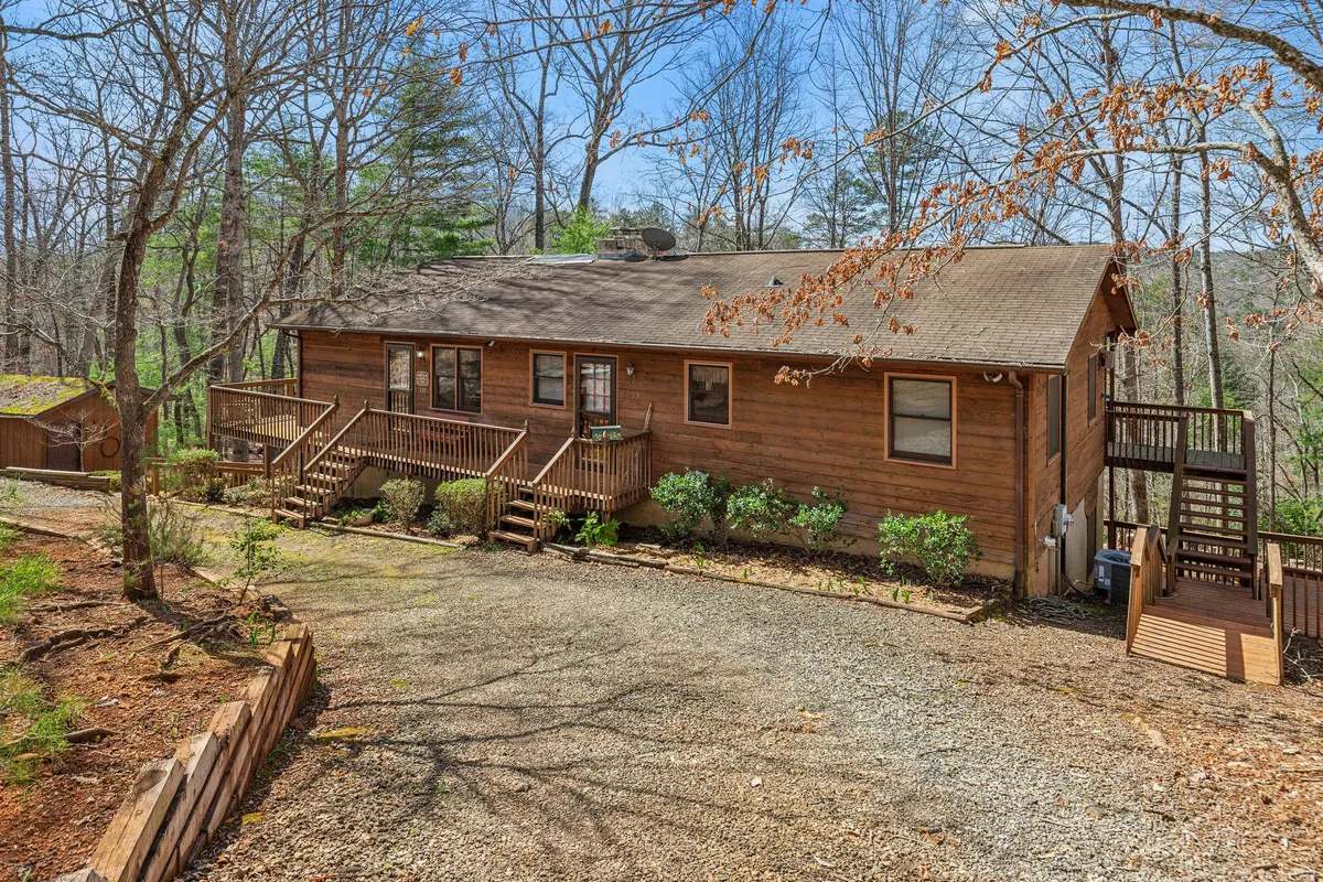 A peaceful exterior shot of the cabin, showcasing its inviting wooden façade, staircase, and gravel driveway nestled among mature trees. The natural setting emphasizes access to nature walks and family barbecues, reinforcing the spirit of outdoor adventure.