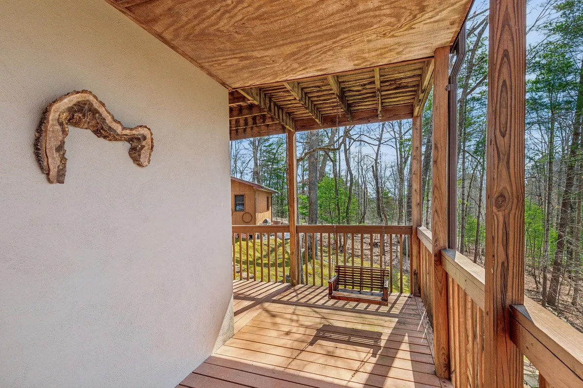 A peaceful exterior scene featuring a classic wooden swing hanging from a sturdy frame, surrounded by lush trees and natural greenery. The swing faces outward, providing a serene spot to sit and take in the beauty of the outdoors. The exterior wall behind the swing is adorned with colorful wall art, enhancing the welcoming and creative atmosphere.