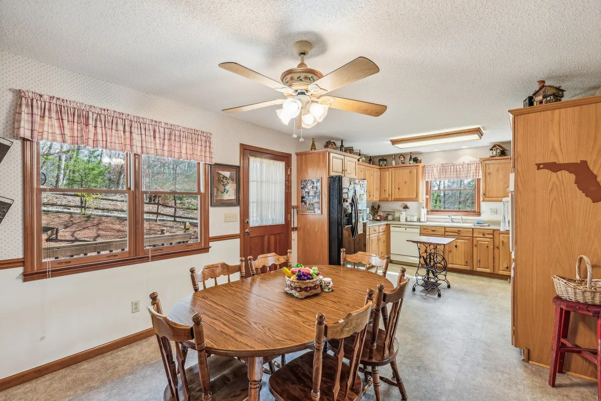 A wide view of the kitchen and dining area shows a spacious wooden table, well-equipped kitchen cabinets, and large windows offering views and natural light. The ambiance is cozy and welcoming, suitable for family meals or group celebrations.