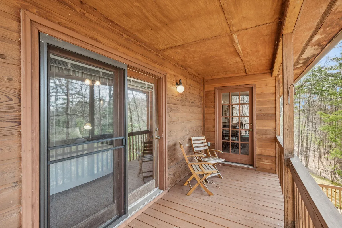 A tranquil wooden deck with glass doors opening from the house, furnished with comfortable outdoor seating amidst a natural backdrop. The viewpoint provides a sense of seamless indoor-outdoor flow, inviting moments of lounging and enjoying the gentle sounds of nature.