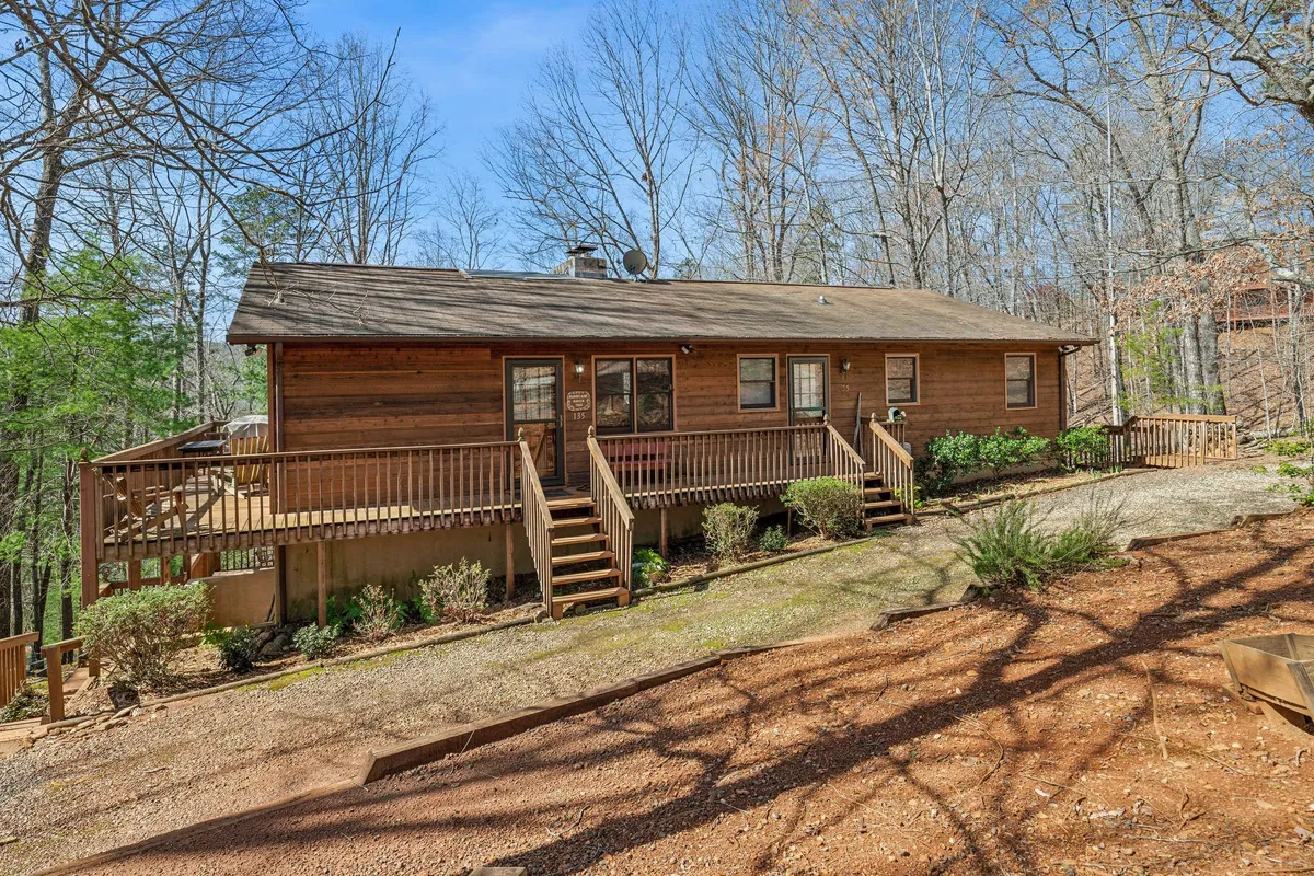 This image features a wooden deck nestled among mature trees, with front steps leading up and outdoor seating available. The scene is peaceful and welcoming, perfectly illustrating the idea of an expansive deck surrounded by nature. The visible deck offers ample space for gatherings, coffee sipping, or quiet relaxation.