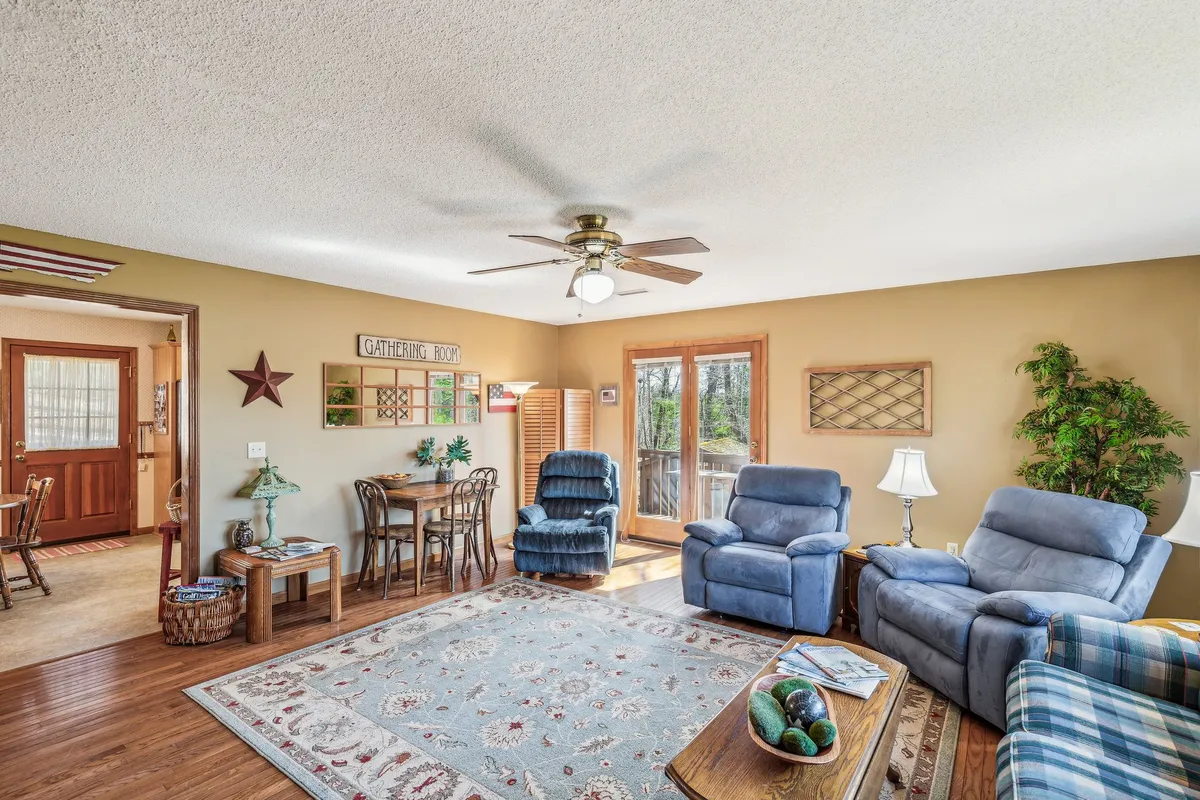 A cozy interior scene with blue recliners, a wooden dining table perfect for card games, and decorative wall art. The welcoming arrangement invites guests to unwind or enjoy a casual game night together.