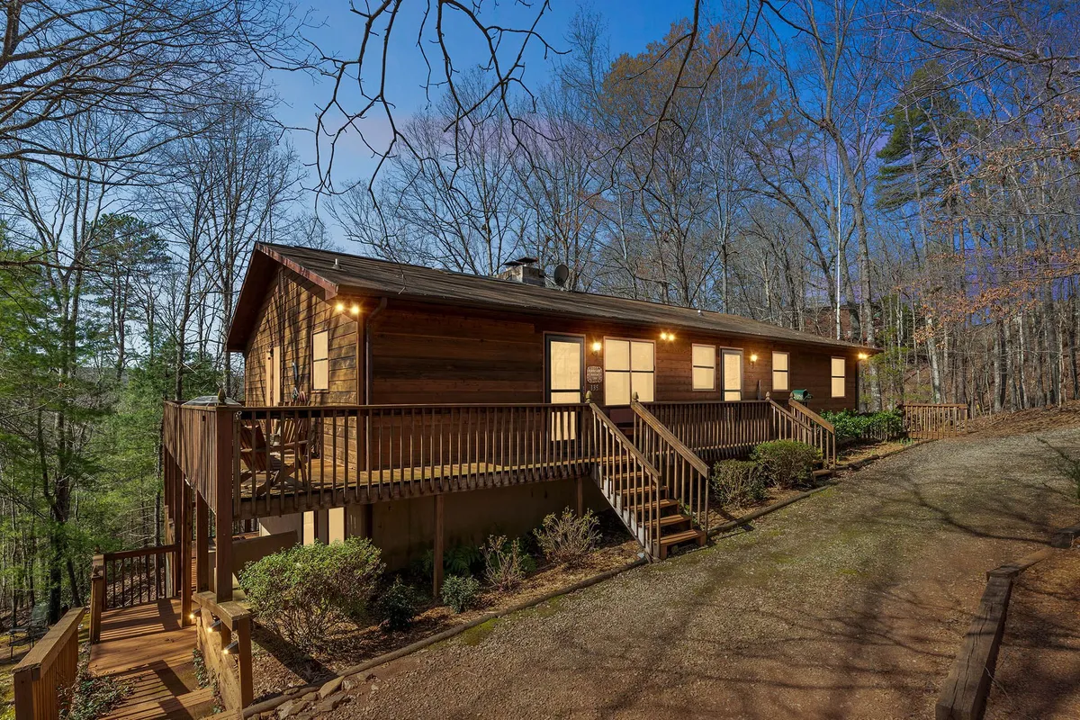 A serene view of the wooden deck extending from Hurricane Haven, framed by large windows and surrounded by lush trees. The inviting outdoor space looks ready for family gatherings, stargazing, and easy access to nature trails just beyond the deck.