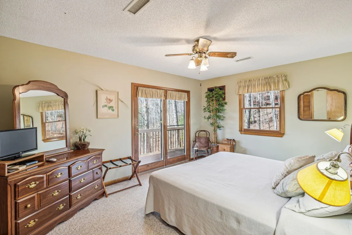 A welcoming bedroom featuring a cozy bed, a wooden dresser, a window with a pleasant view, a leafy green plant, and a comfortable chair. Natural light streams in, suggesting a peaceful connection to the outdoors and an inviting spot for relaxation or reading.